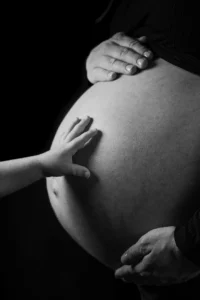 Close-up of a pregnant woman’s belly with a child’s hand touching it, symbolizing pregnancy and individuals who should avoid anti-wrinkle injections like Botox.