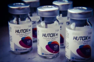 Close-up of several HUTOX INJ vials containing 100 units of Clostridium Botulinum Toxin Type A, produced by Huons Global, arranged on a table.