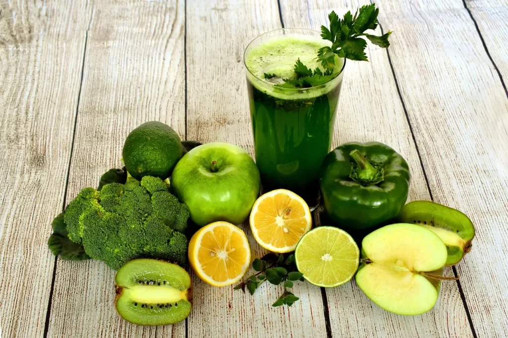 Fresh green fruits and vegetables rich in antioxidants including broccoli, kiwi, apple, and lemon with a green juice
