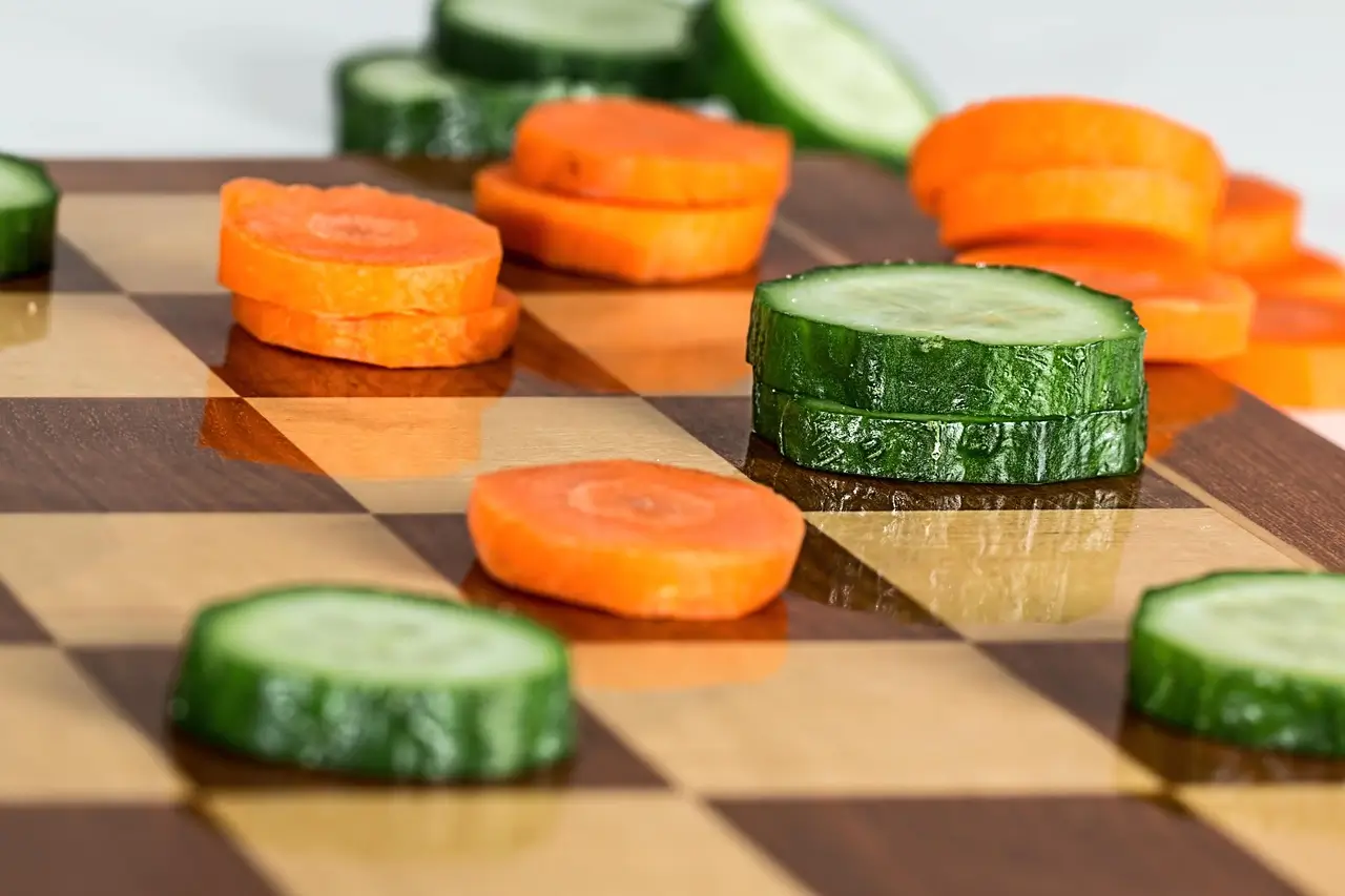 Slices of carrot and cucumber arranged creatively on a chessboard symbolizing healthy eating and a balanced diet.