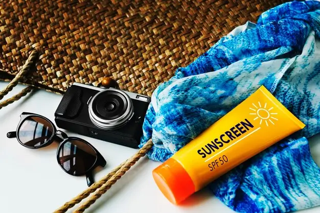 SPF 50 broad-spectrum sunscreen tube on a beach towel beside sunglasses and a camera