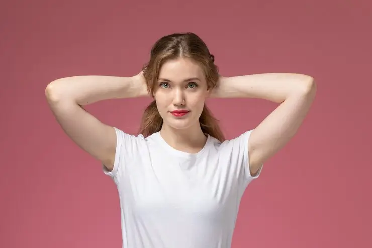 Confident woman lifting her arms to show smooth underarms after laser hair removal, standing against a pink background — representing clearer, brighter skin and reduced ingrown hairs after treatment.