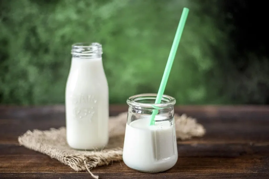 Fresh and delicious coconut milk served in glass bottles with a green straw on a wooden table, representing healthy plant-based nutrition.