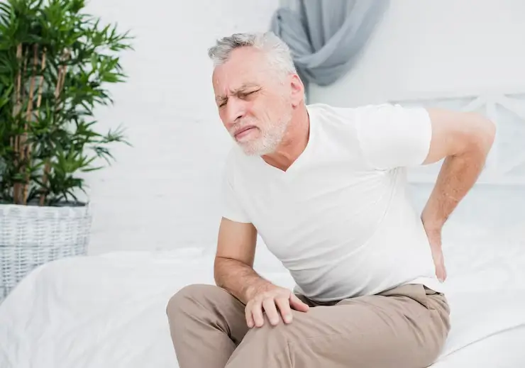 Elderly man holding his lower back while experiencing back pain