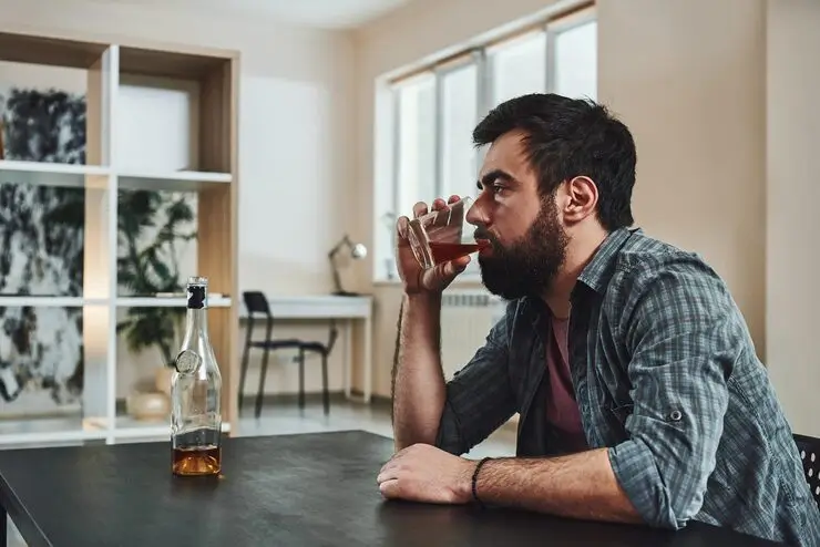 Man sitting at a table drinking alcohol from a glass, illustrating how alcohol consumption leads to alcohol breath.