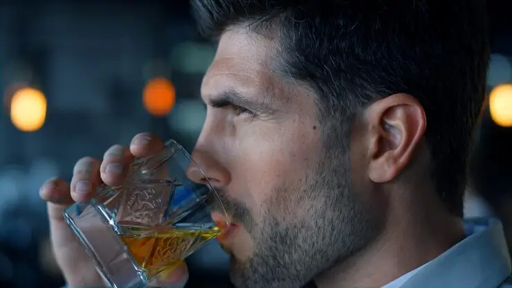 Close-up of a man drinking whiskey from a glass, showing how alcoholic drinks contribute to alcohol breath.