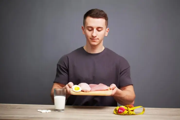 Young man sitting at a table holding a plate with meat and an egg beside a glass of milk, representing a high-protein diet for healthy hair.