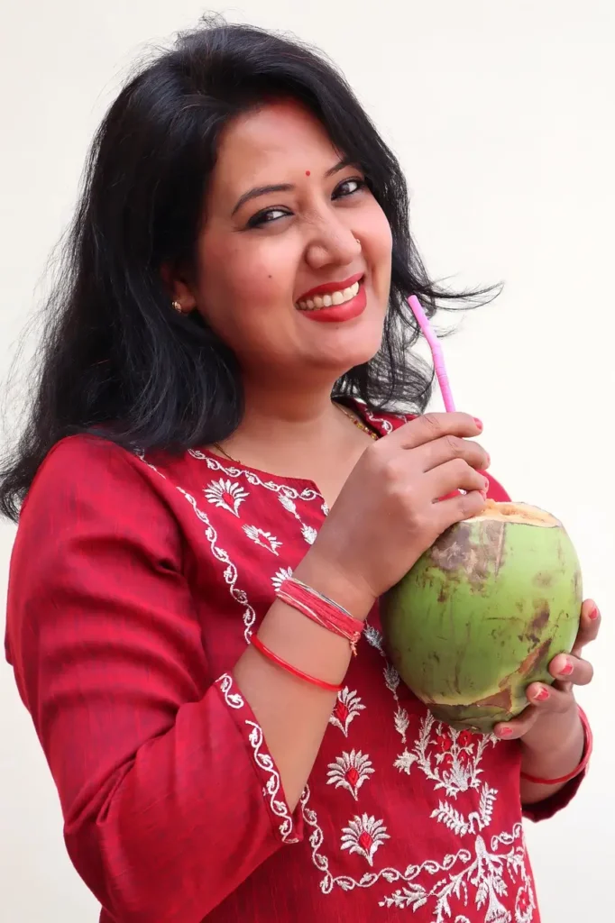 Woman smiling while drinking fresh coconut milk, showing the health benefits of coconut milk.