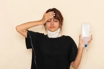 Sick woman holding an IV fluid bag and touching her forehead while feeling unwell