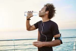 A person drinking water while jogging by the sea, promoting the importance of staying hydrated for a healthy lifestyle.