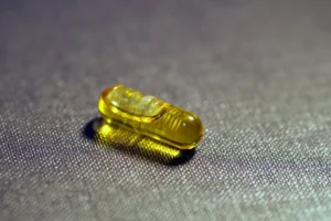 A yellow vitamin D capsule placed on a textured surface, representing vitamin D supplements for bone and immune health.