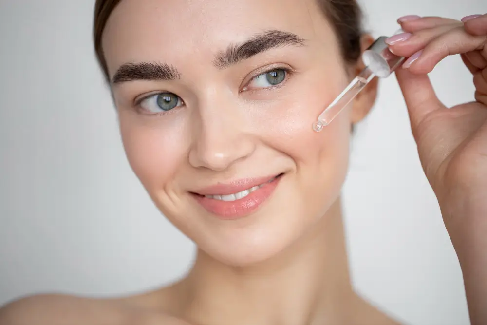 Close-up of a woman applying facial serum with a dropper, illustrating skincare steps using vitamin C or retinol.