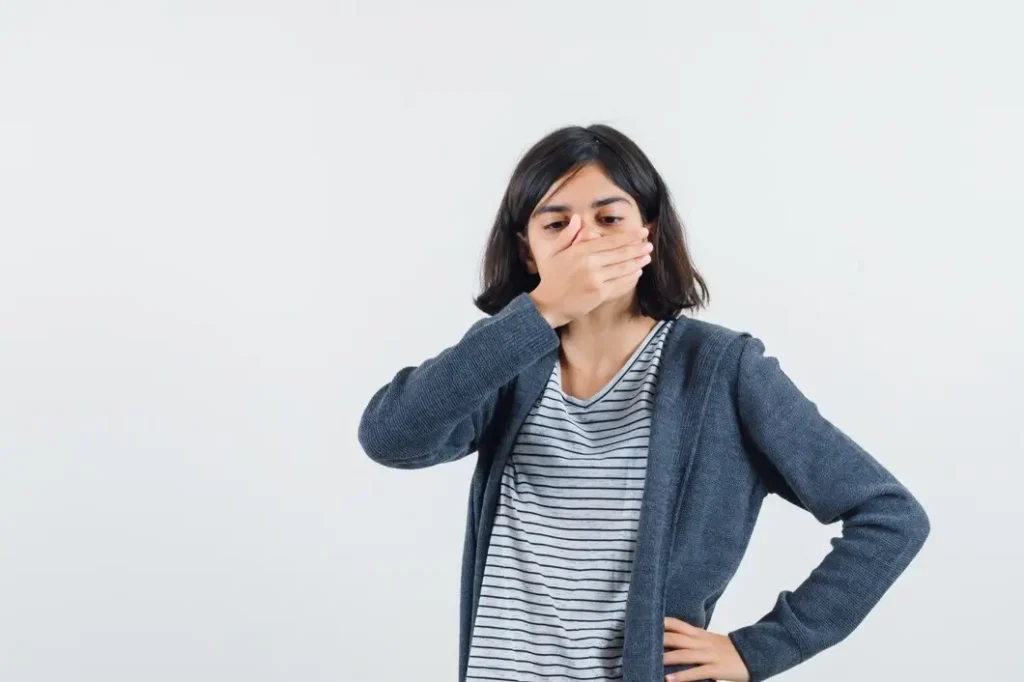 Young woman covering her mouth because of bad breath which may be caused by cavities
