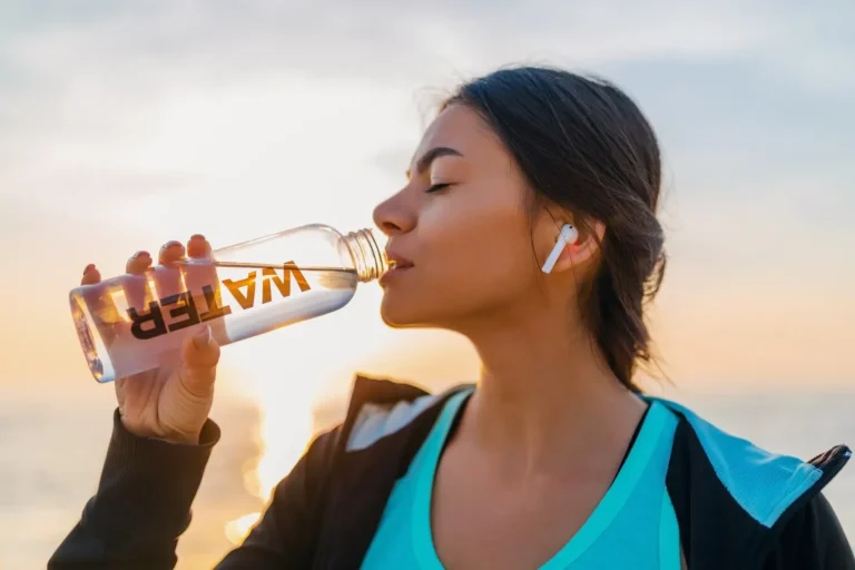 Woman drinking water from a bottle at sunset to stay hydrated