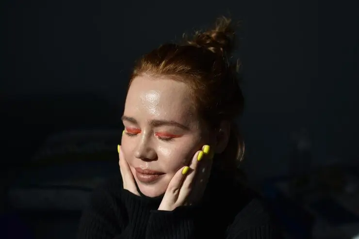 Woman with glowing, dewy skin sitting in sunlight with her eyes closed, showing the results of a consistent vitamin C and retinol skincare routine.