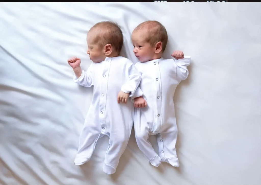 Identical twin babies lying side by side in white outfits, featured on BilalMD.com Twin Calculator page to represent identical twin pregnancy